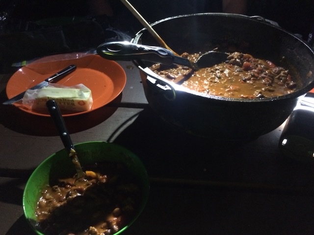 Camp meal cooking at night with a light beside the pot